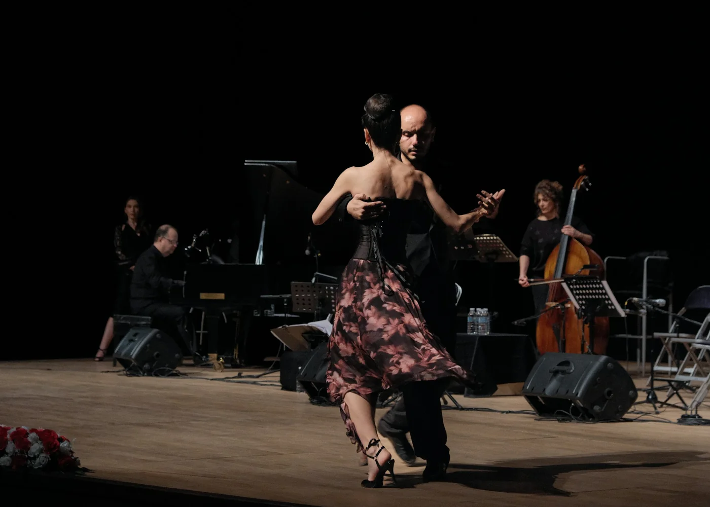 A tango couple dancing on stage in front of a live orchestra with piano and double bass, representative of Tango Porteño's live-music production
